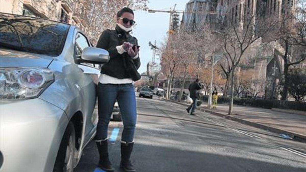 Una joven utiliza el móvil, el viernes, en la zona azul de pago inteligente en la calle de Provença, frente la Sagrada Família.