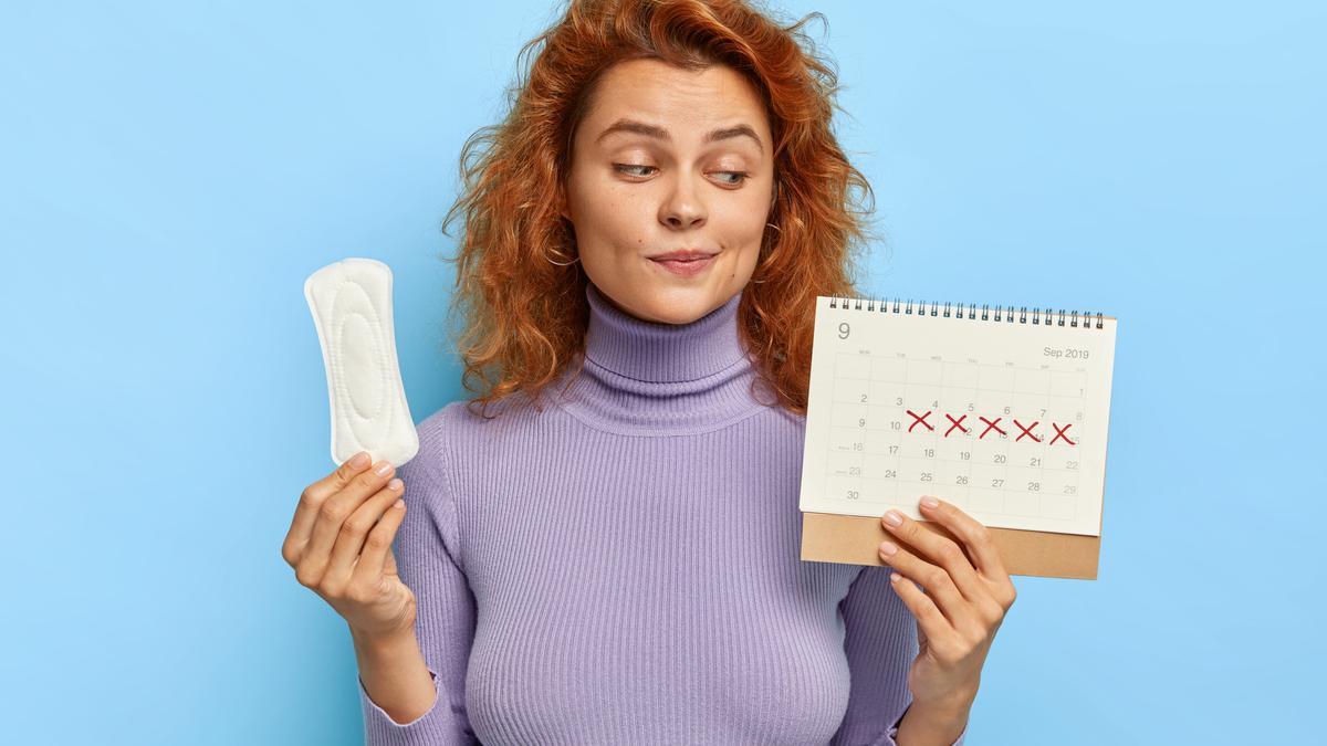 Una mujer mira su calendario menstrual y sujeta una compresa