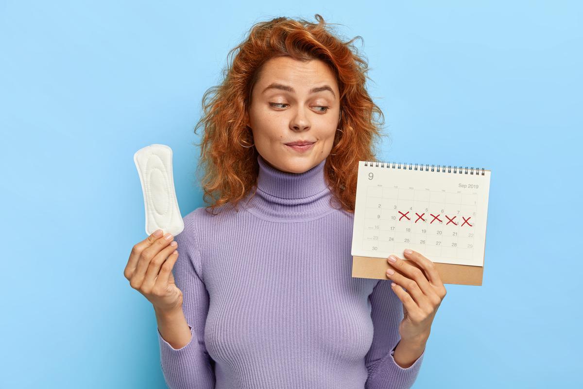 Una mujer mira su calendario menstrual y sujeta una compresa