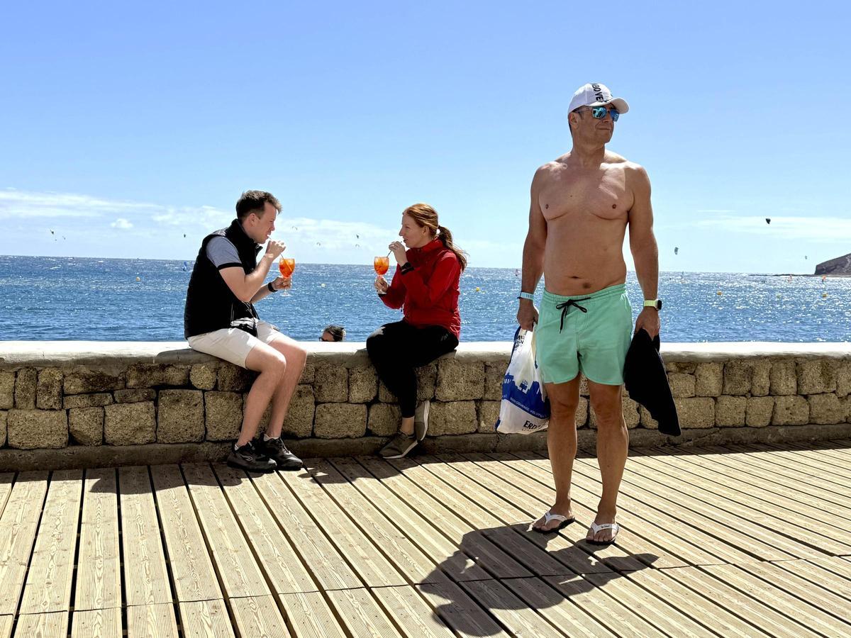 En la imagen, inspirada por el fotógrafo británico Martin Parr, dos turistas disfrutan de un Aperol Spritz junto al mar, mientras otro turista descamisado les roba el protagonismo