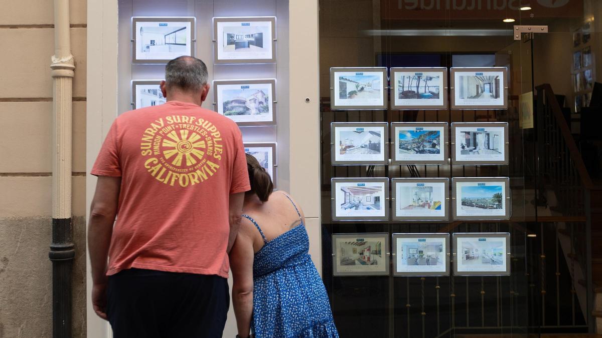 Dos personas observan las ofertas en el escaparate de una inmobiliaria.