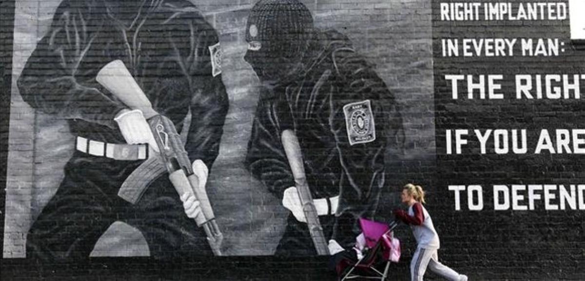 Una dona amb un cotxet de criatura passa davant d’un mural de paramilitars unionistes, a l’est de Belfast, aquest dimecres.