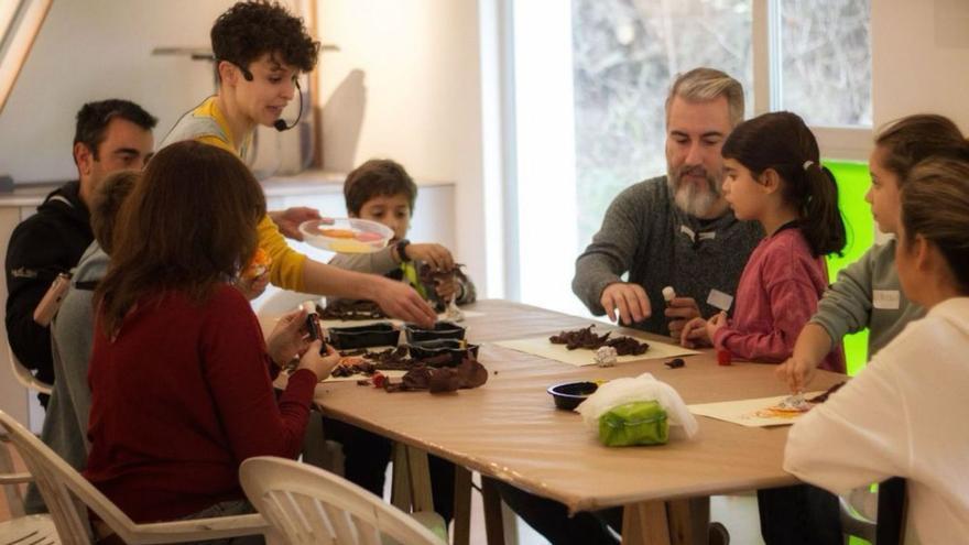 La coordinadora del taller junto a un grupo de padres y niños haciendo manualidades. | Alba Prieto