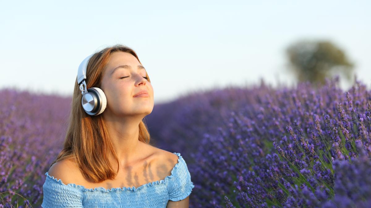Mujer con auriculares respirando aire fresco escuchando música en un campo de lavanda