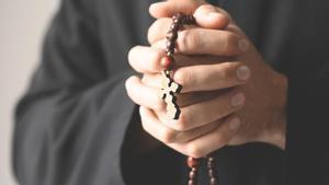 Las manos de un sacerdote sostienen un rosario