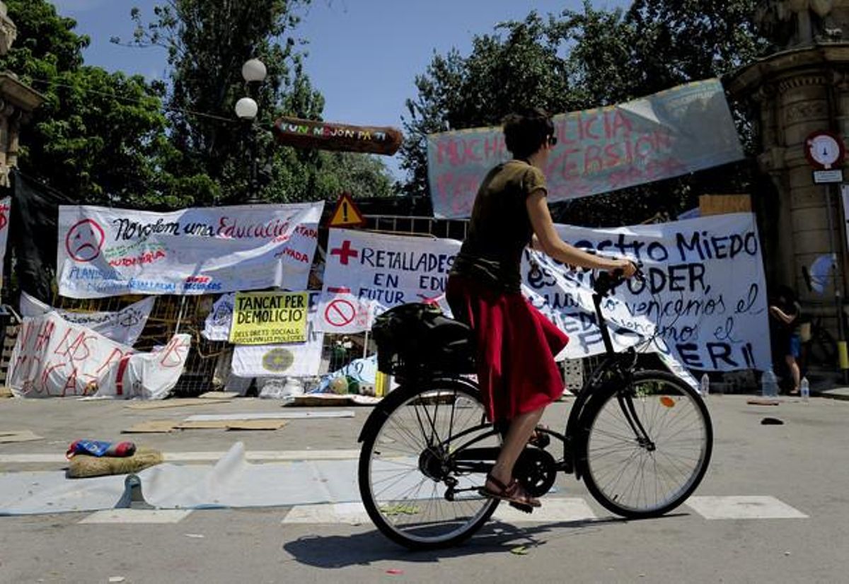 Una dona passa en bicicleta davant la porta principal del parc de la Ciutadella, coberta de pancartes de protesta dels indignats.