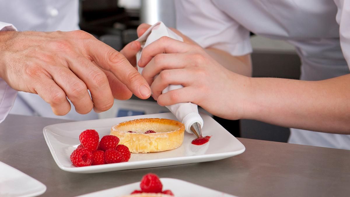 Un primer plano de un chef enseñando a un joven aprendiz de cocina Un primer plano de un chef enseñando a un joven aprendiz de cocina