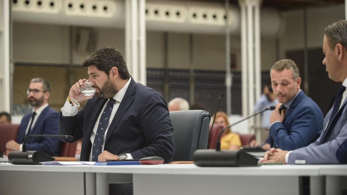 López Miras bebe agua en una sesión plenaria de la Asamblea Regional. A su espalda, el portavoz del Grupo Popular, Joaquín Segado.
