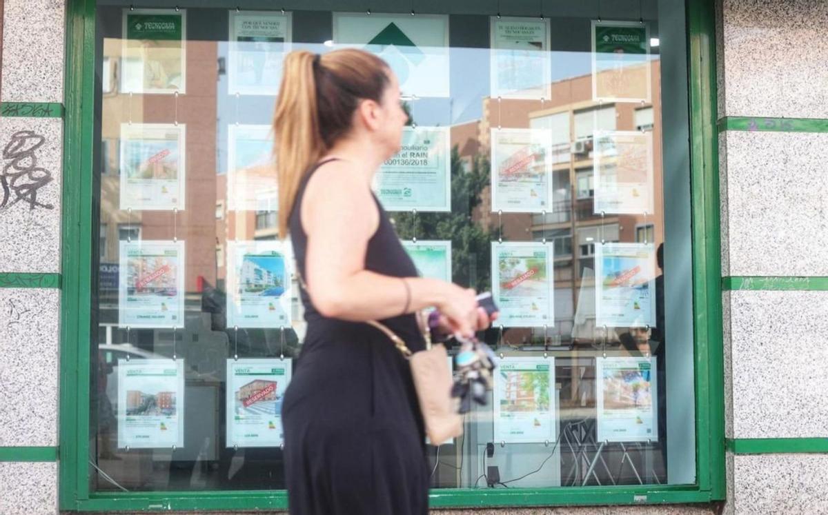 Una mujer pasa por delante de un escaparate con los anuncios de una inmobiliaria. | ÁLEX ZEA