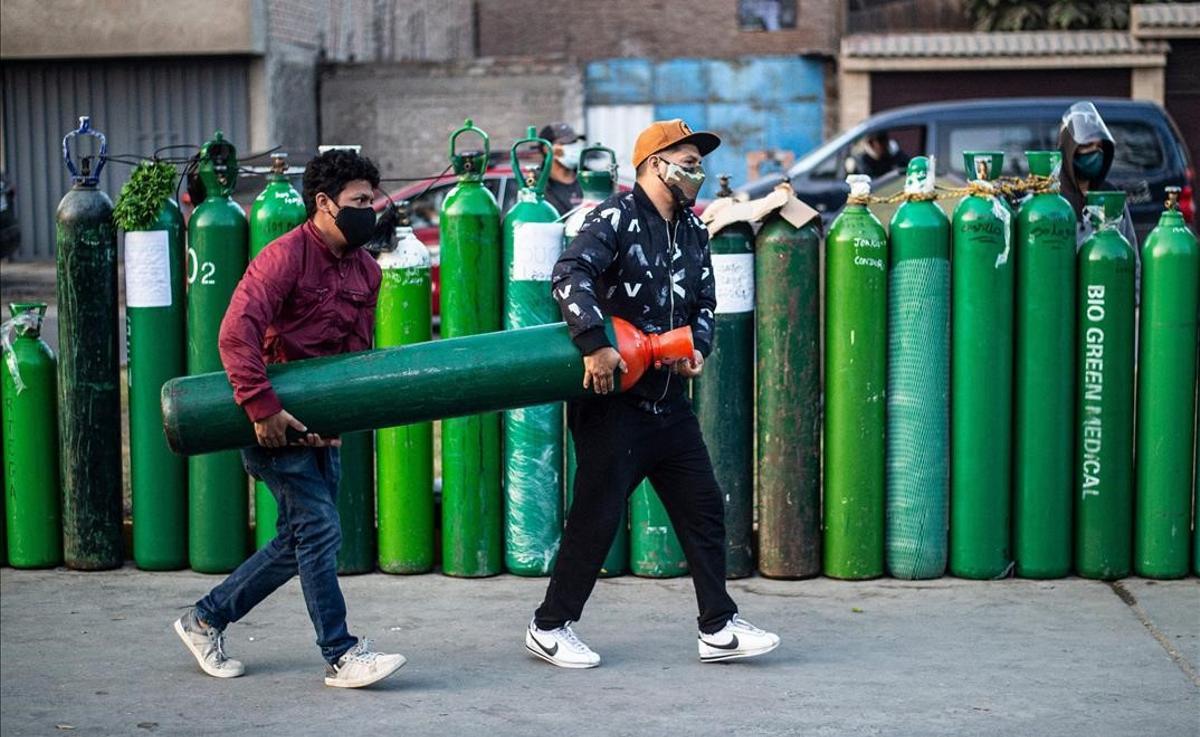 Dos hombres cargan con la botella de oxígeno para poderla rellenar en Callao (Perú).