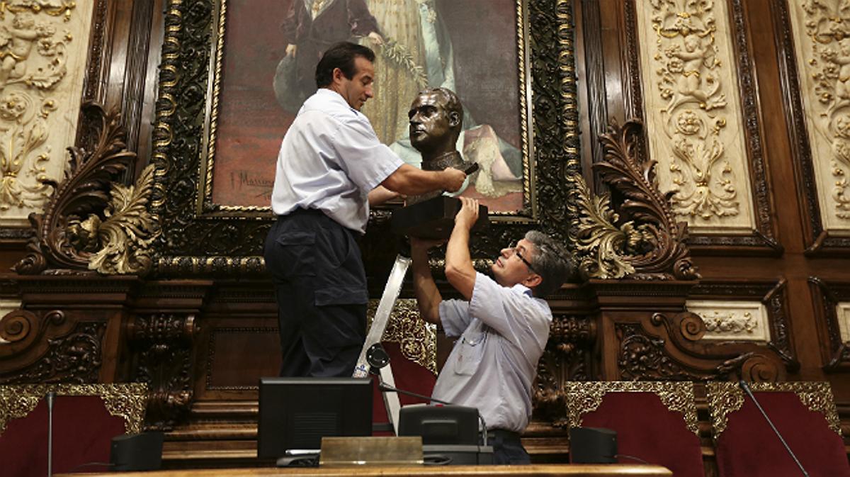 Dos operaris retiren el bust del rei Joan Carles del saló de plens de l’Ajuntament de Barcelona.