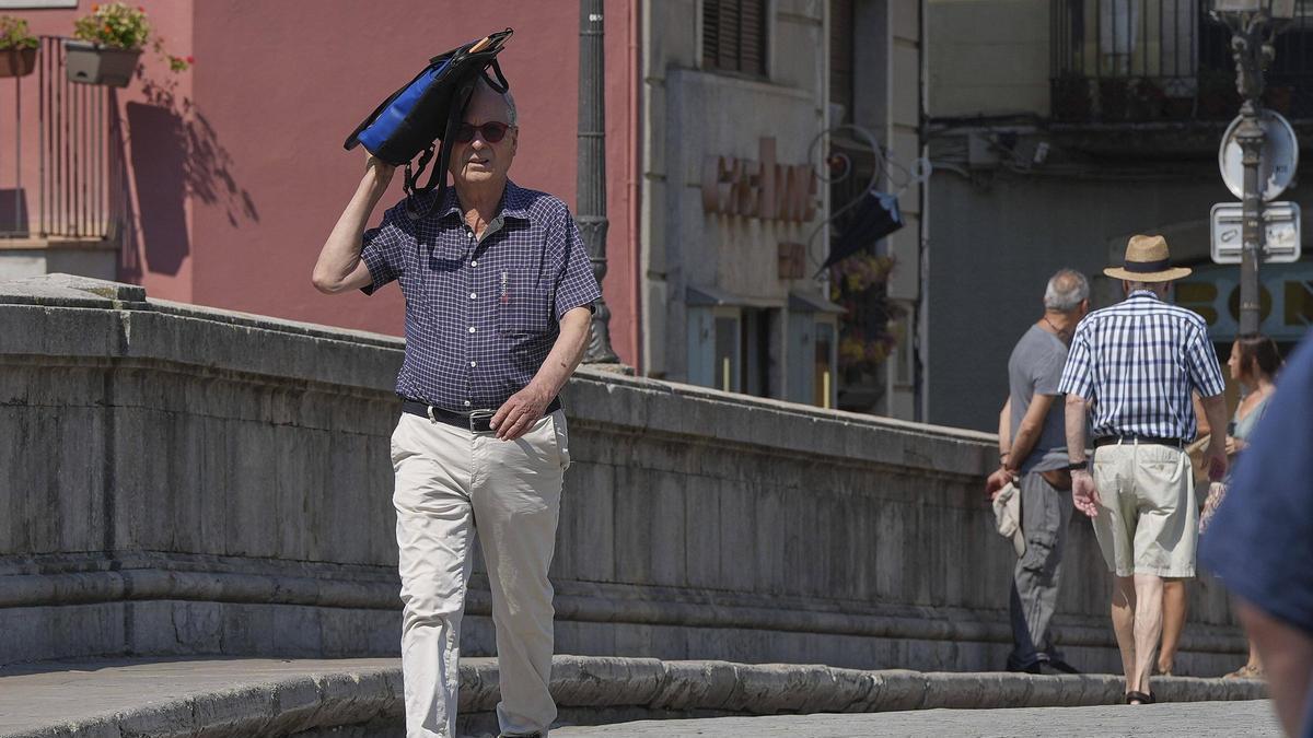 Un vianant es protegeix del sol en plena onada calor a Girona.