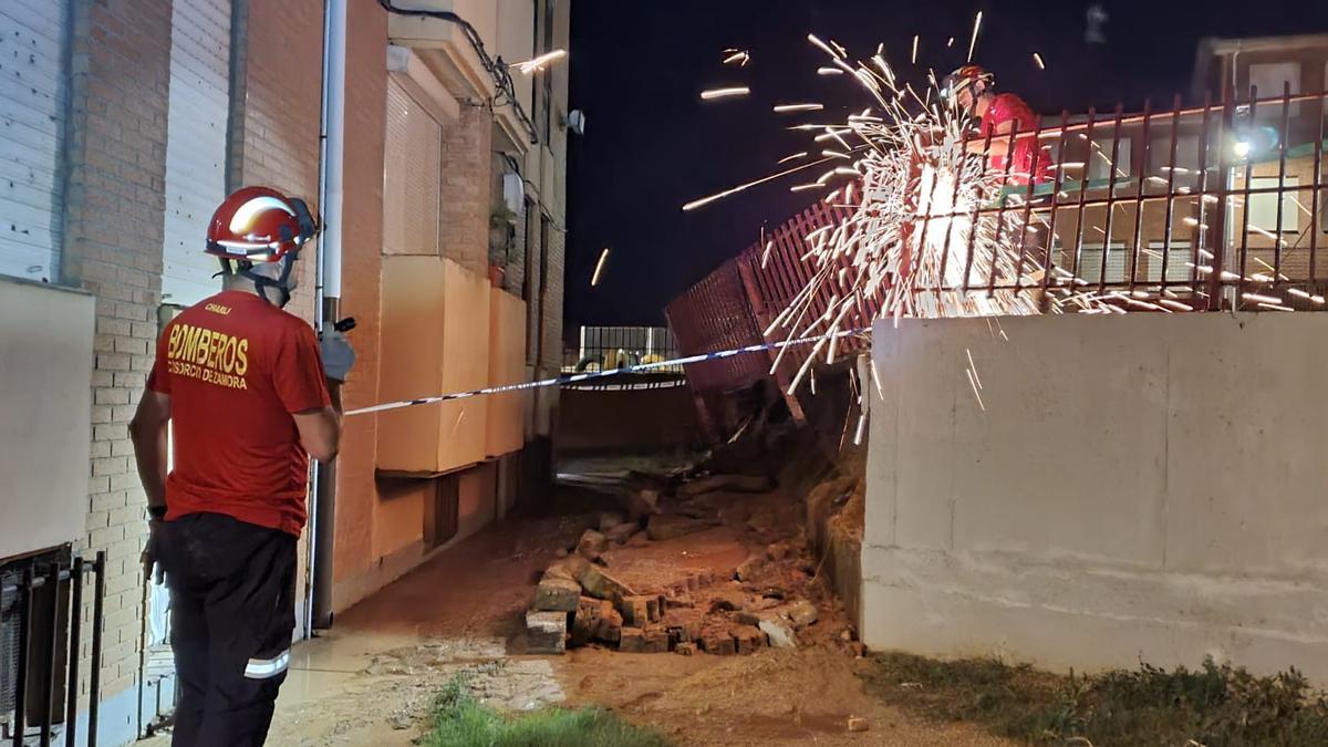 Los bomberos cortando un tramo de valla de seguridad desplazada y desencajada por el movimiento de tierras.