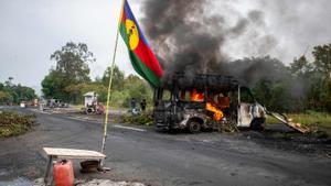 Una bandera kanak ondea junto a un vehículo en llamas en un puesto de control independentista en La Tamoa, comuna de Paita, el pasado domingo. (Photo by Delphine Mayeur / AFP)