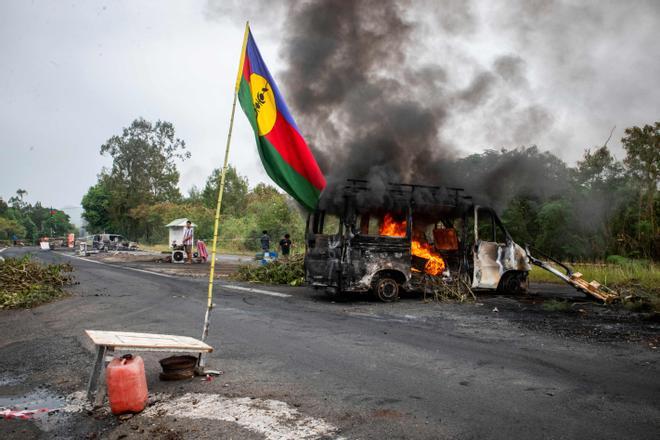 Una bandera kanak ondea junto a un vehículo en llamas en un puesto de control independentista en La Tamoa, comuna de Paita, el pasado domingo. (Photo by Delphine Mayeur / AFP)