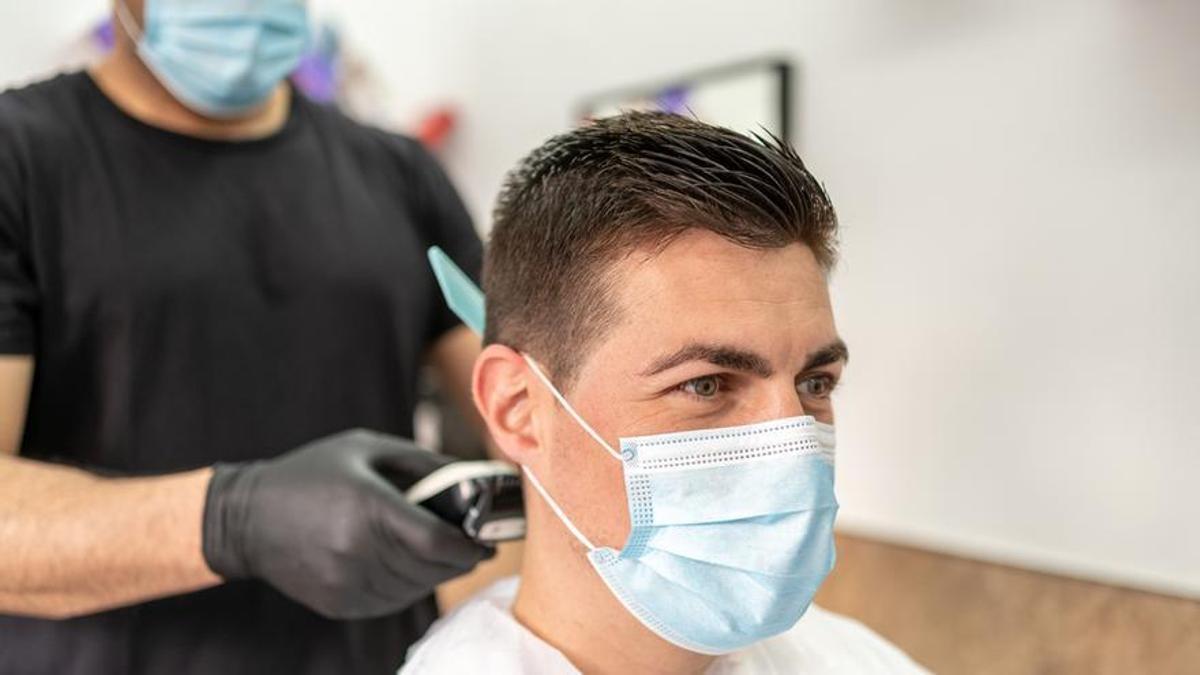 Un peluquero corta el pelo a un joven.