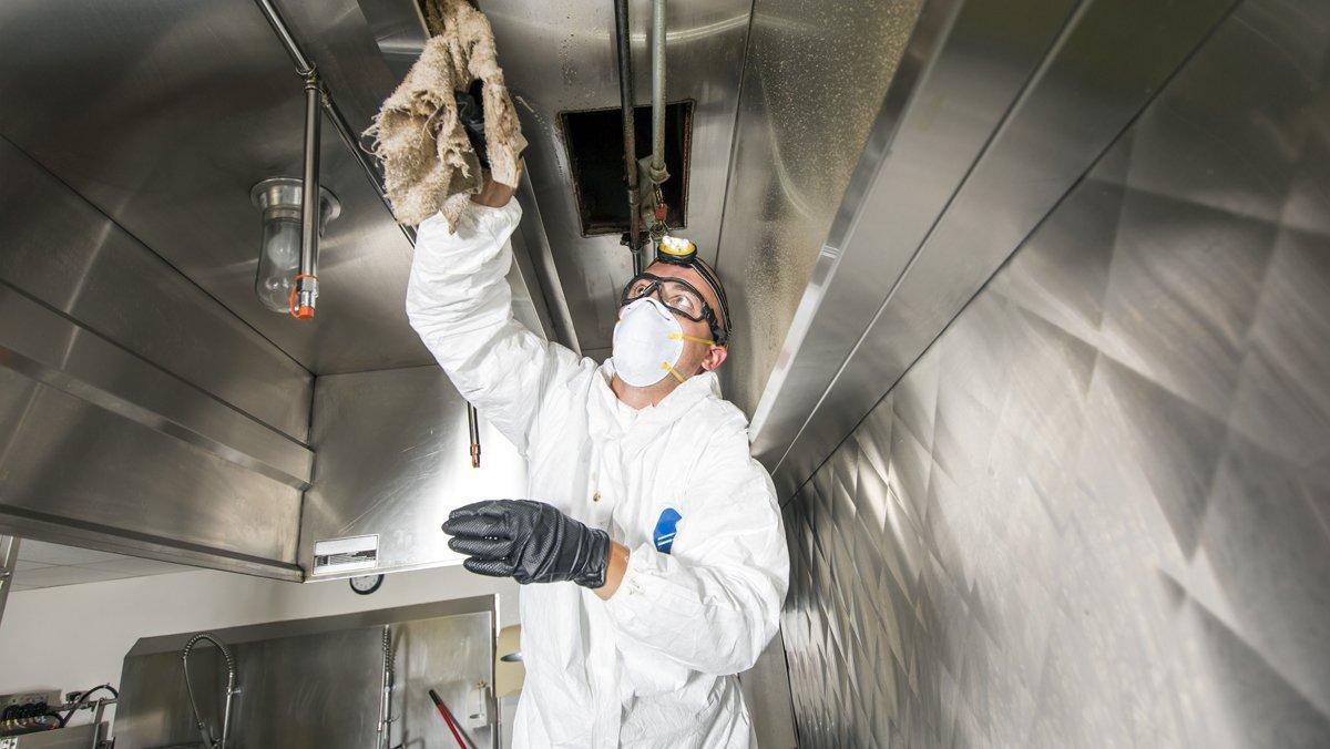 A Commercial kitchen worker washing up at sink in professional clothes