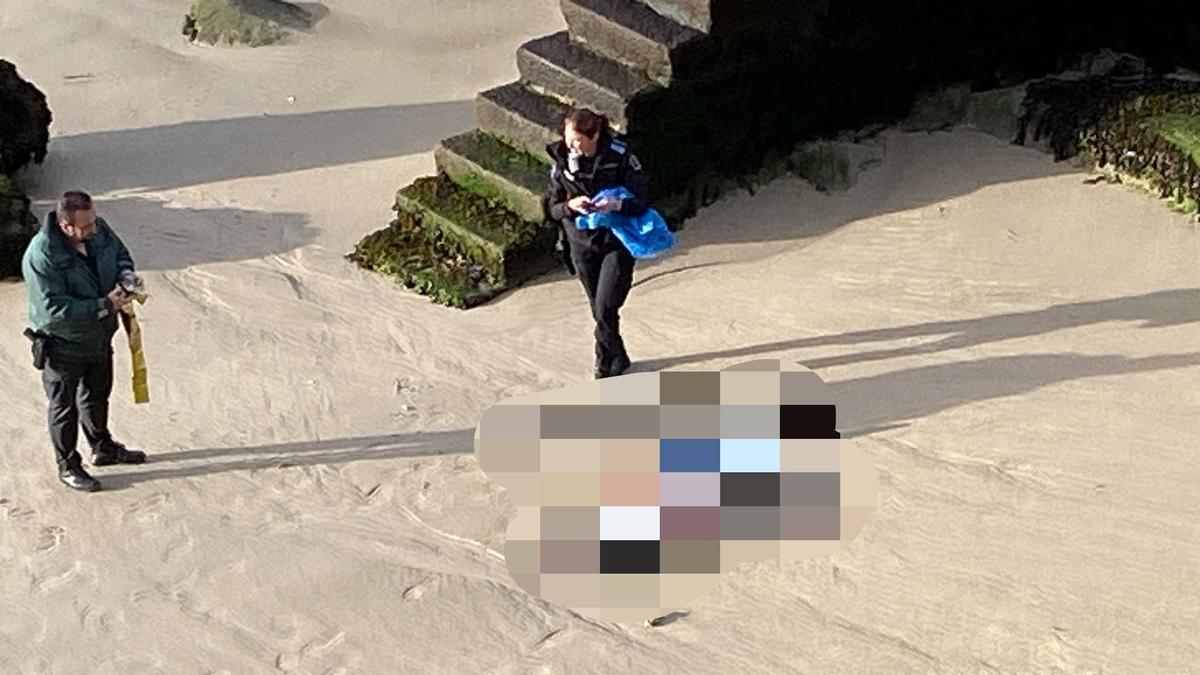 Un guardia civil y policía local junto al cuerpo sin vida que apareció en la playa en Domaio.