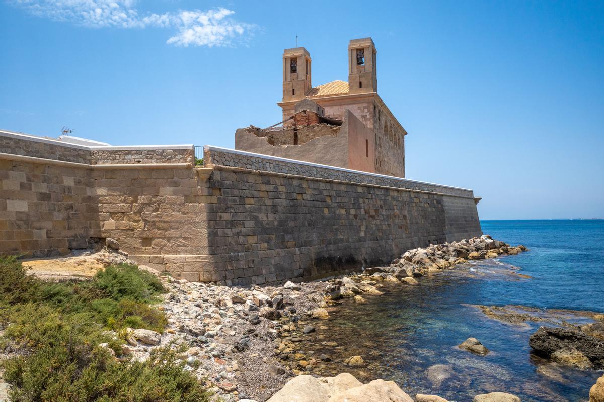 Histórica iglesia de piedra junto al mar bajo un cielo azul claro en la isla de Tabarca, España