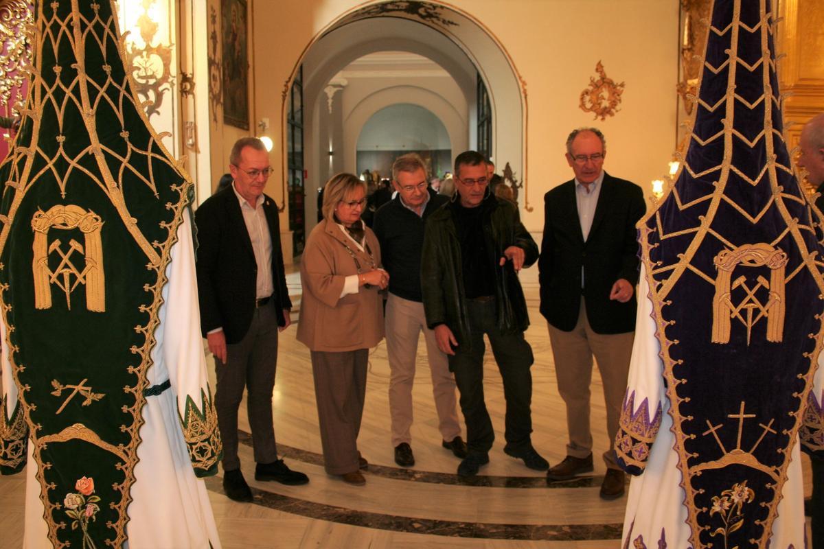 El presidente del Paso Blanco y la presidenta del Coro de Damas de la Virgen de la Amargura, junto a tres de los hijos de Antonio Felices Iglesias, examinan detalles de los nazarenos de la exposición.