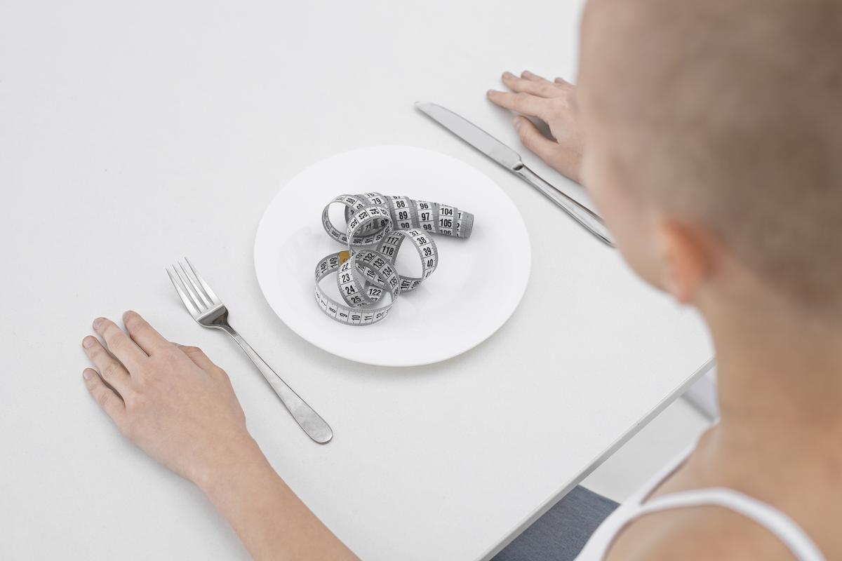 mujer joven trastorno alimentario cinta metrica plato