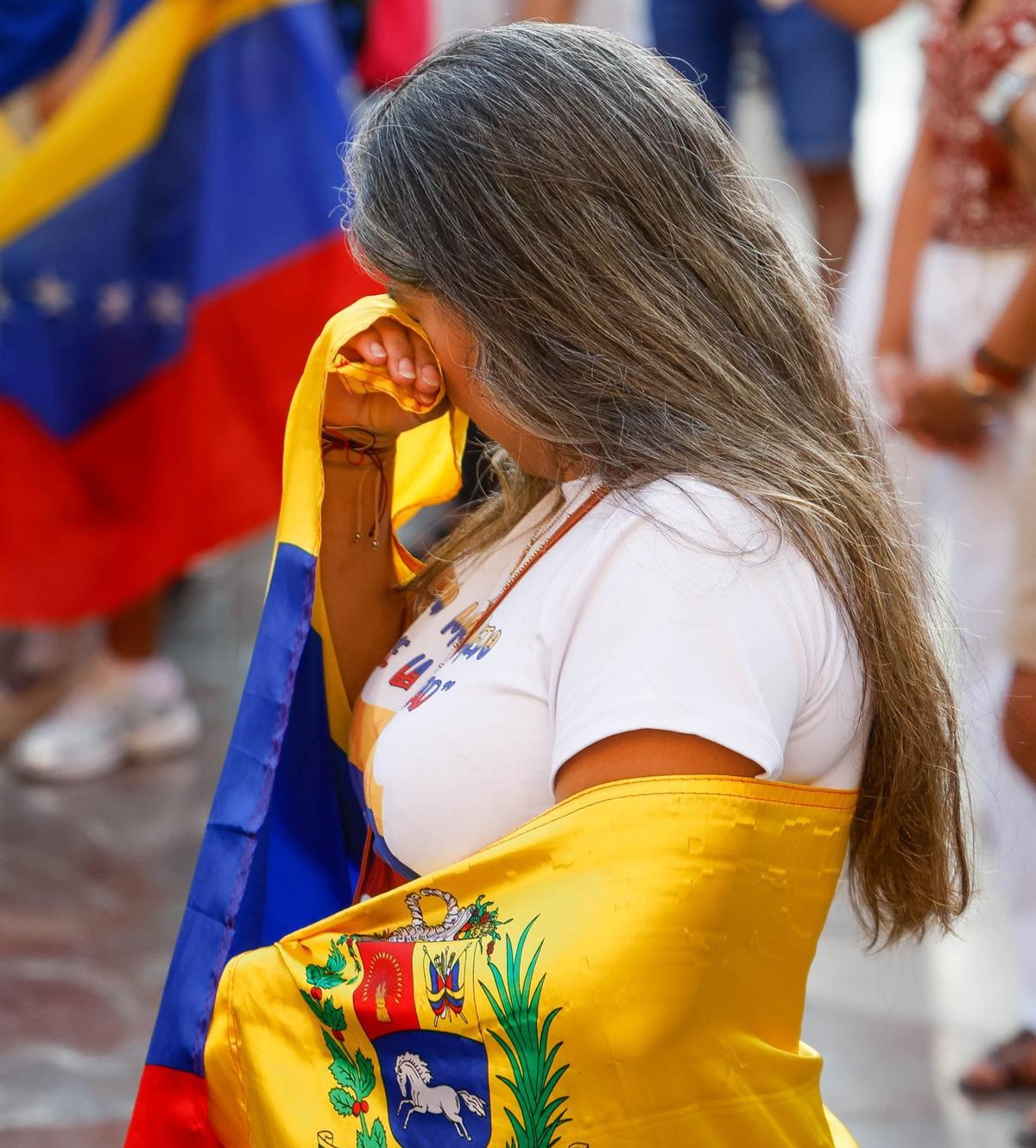 Una mujer rodeada conla bandera venezolana no puede contener las lágrimas en València.
