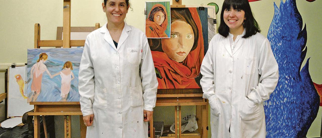 Natalia Capellán y Leticia Rodríguez, con varios cuadros y pinturas detrás.