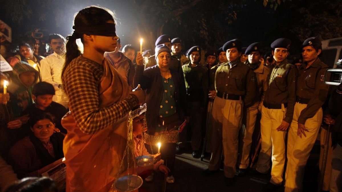Una mujer con los ojos vendados en una vigilia en protesta por las violaciones en India ante la atenta mirada de las fuerzas del orden en Nueva Delhi