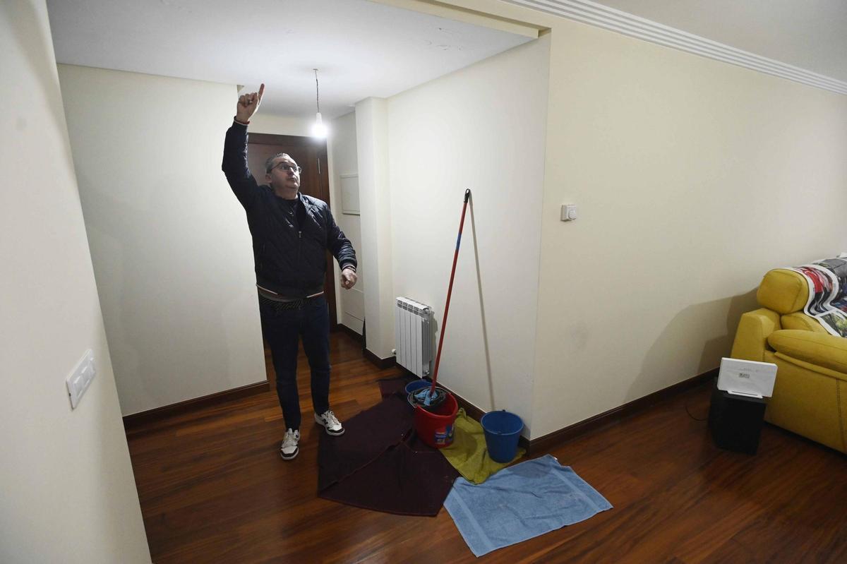 Alfonso señala las humedades en el techo de su salón, con cubos, toallas y fregonas.