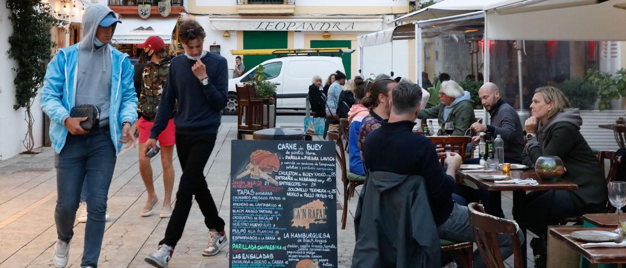 Dos jóvenes pasan por delante de la terraza de un bar en el barrio de La Marina.