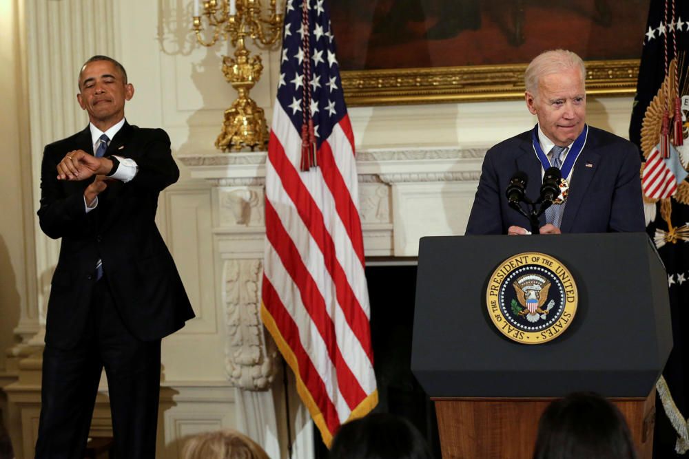 Barack Obama mira su reloj a modo de broma al ver lo que se alarga el discurso del vicepresidente Joe Biden en la Casa Blanca, en Washington.