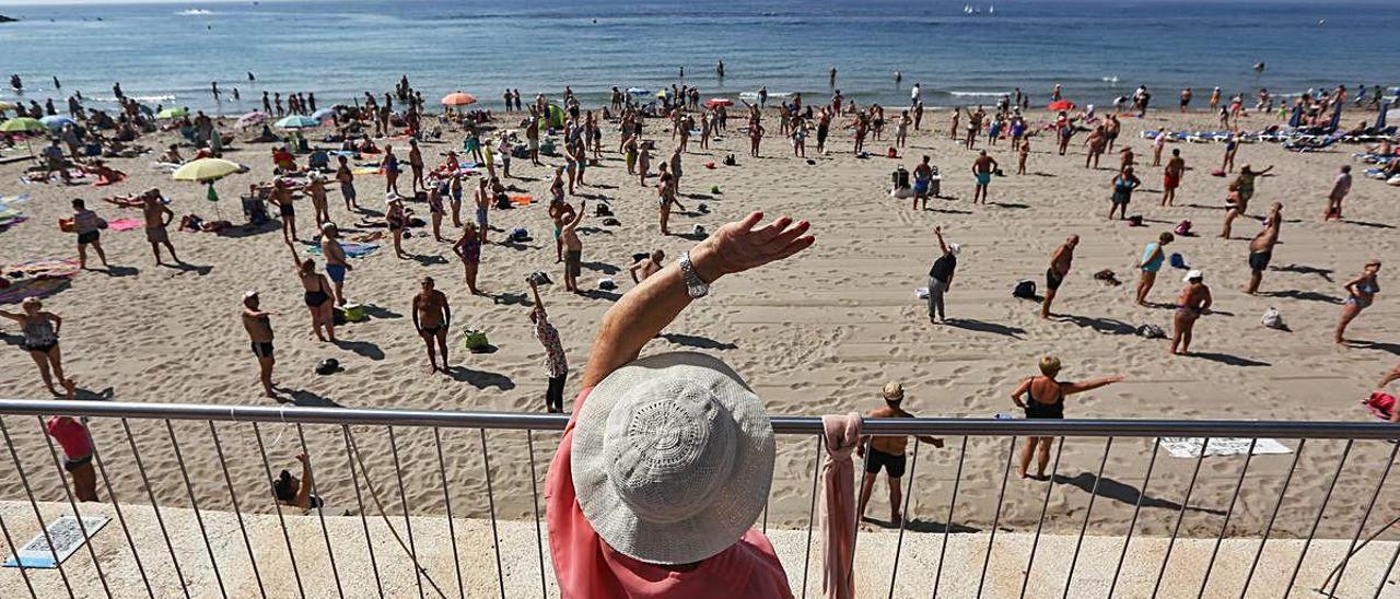 Una mujer observa desde el paseo de Levante de Benidorm una sesión de gimnasia de turistas del Imserso el invierno pasado. DAVID REVENGA