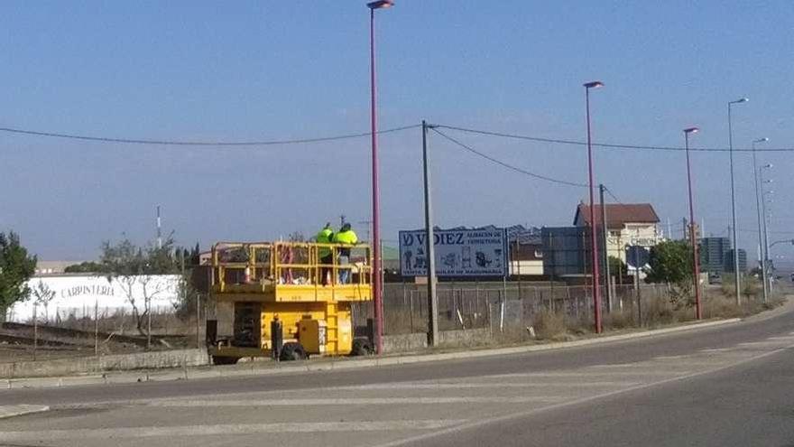 Dos operarios se disponen a renovar las luminarias de una de las farolas del acceso al polígono.