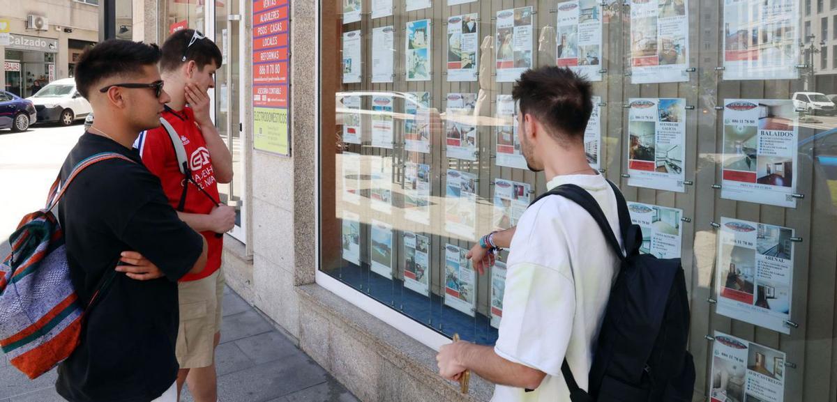 Jóvenes ven anuncios de pisos en una inmobiliaria de Vigo.