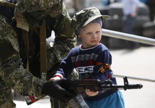 Pro-Russian armed man lends his weapon to a boy posing for a picture for his father in front of the seized town administration building in Kostyantynivka