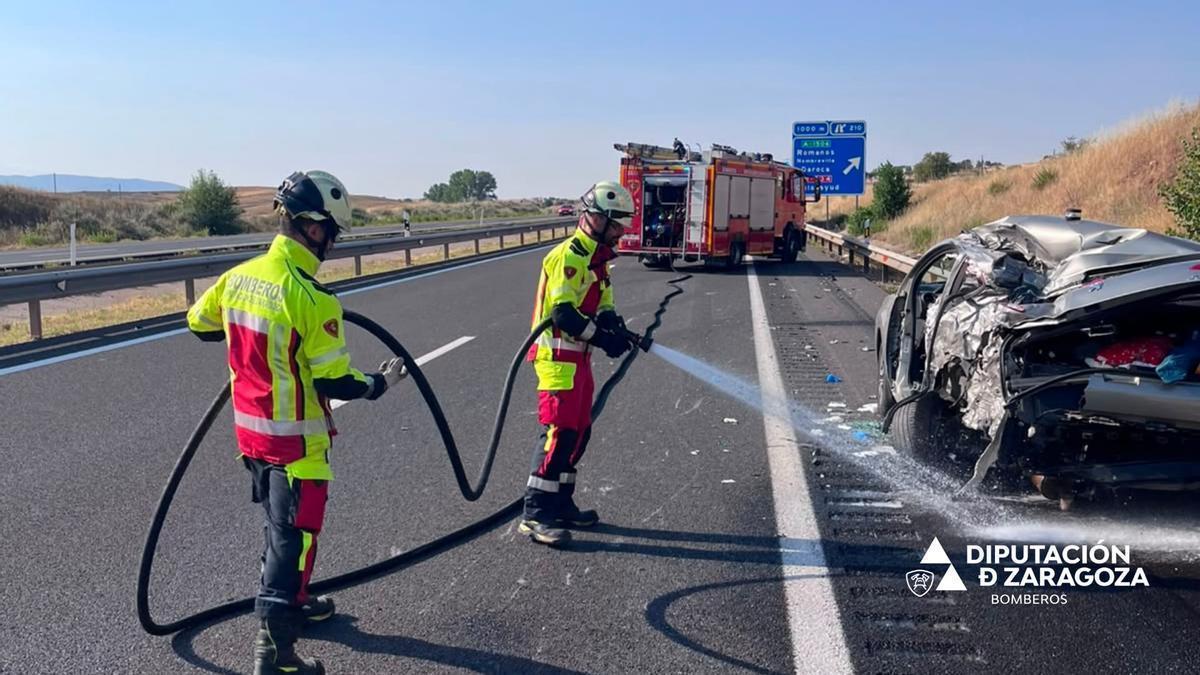 Los bomberos enfrían el vehículo accidentado.