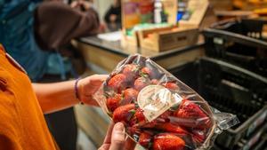 Una mujer observa una bandeja de fresas a punto de caducar en una tienda de Barcelona.
