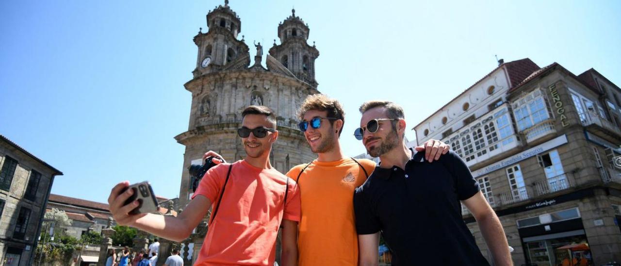 Tres jóvenes turistas se hacen una foto con la iglesia de A Peregrina de fondo.   // GUSTAVO SANTOS