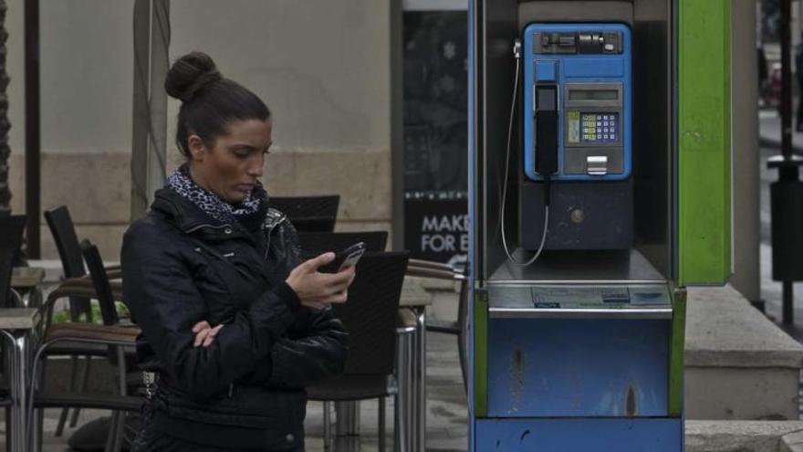 Una joven usa móvil, junto a una cabina telefónica.