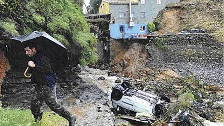 Un hombre pasa junto a un coche arrastrado por la lluvia en Puerto Llampero.