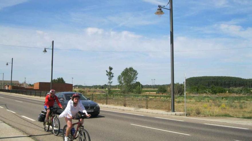 Dos ciclistas en la travesía de Villaveza del Agua donde están instaladas varias farolas.