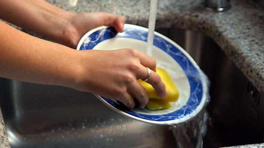 Una mujer lava un plato bajo el grifo.