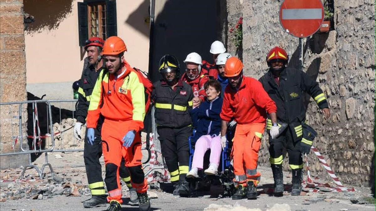 Los bombaros ayudan a una vecina en silla de ruedas a abandonar la localidad italiana de Norcia, afectada por los terremotos.