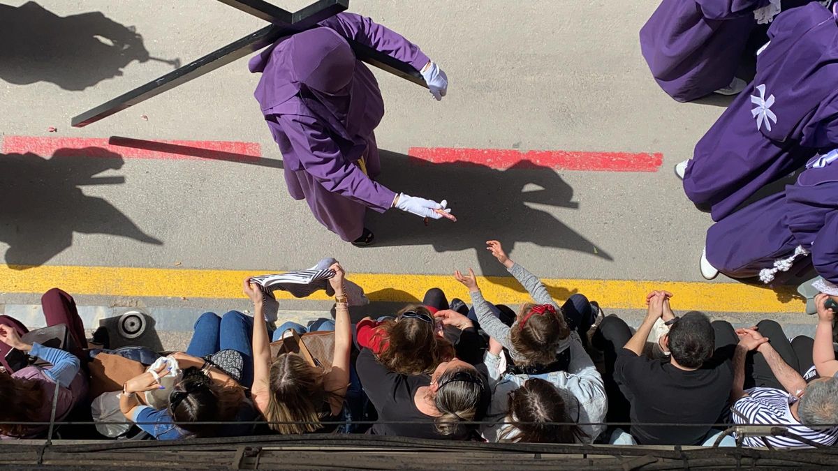 Un nazareno del Viernes Santo da un caramelo a un niño en la procesión de 2022.