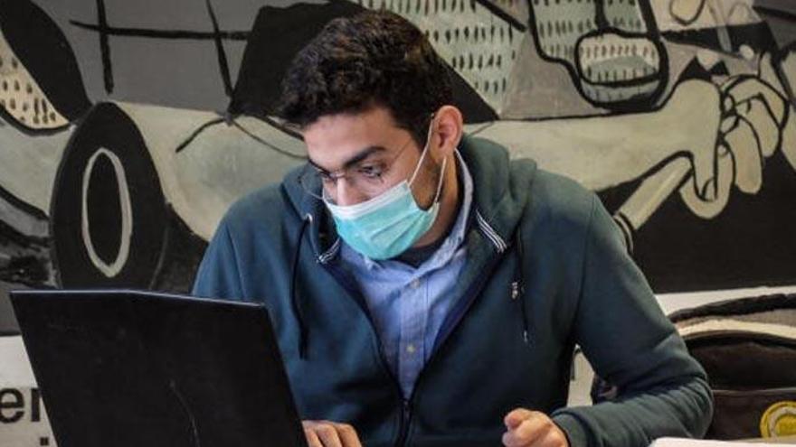 Un joven con mascarilla trabaja con un portátil.