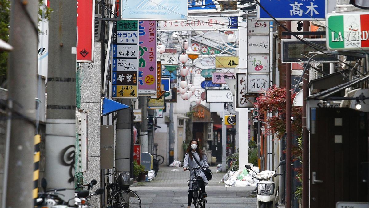 Archivo - Una mujer con mascarilla recorre en bicicleta una calle de Tokio