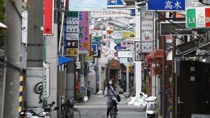 Archivo - Una mujer con mascarilla recorre en bicicleta una calle de Tokio