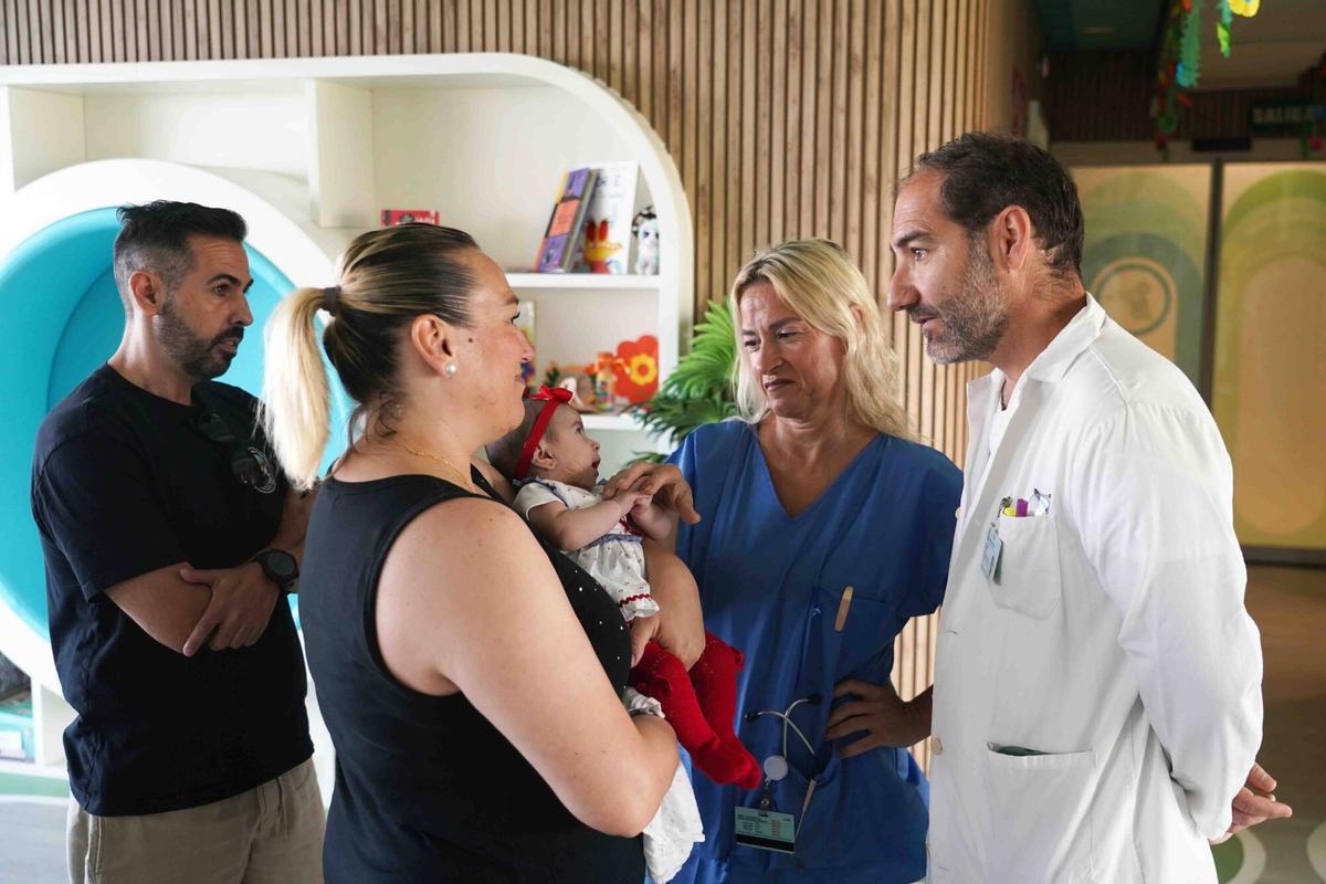 MLG 08-06-2026.-Los padres Rosa María Domínguez y David González, sujetan a su hija Aitana, junto al equipo de médicos de pediatría del Hospital Materno Infantil, donde ha sido operada por un problema de mandíbula.