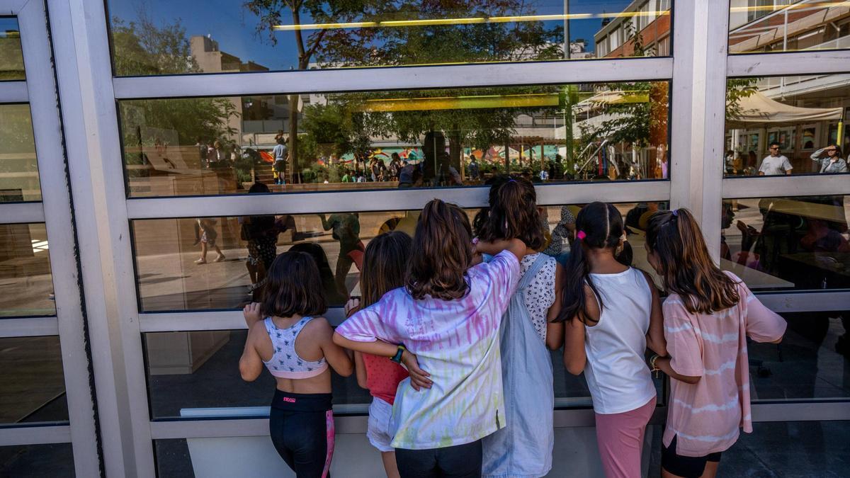 Un grupo de niñas se asoma por una cristalera de su escuela el primer día de clase, este lunes.