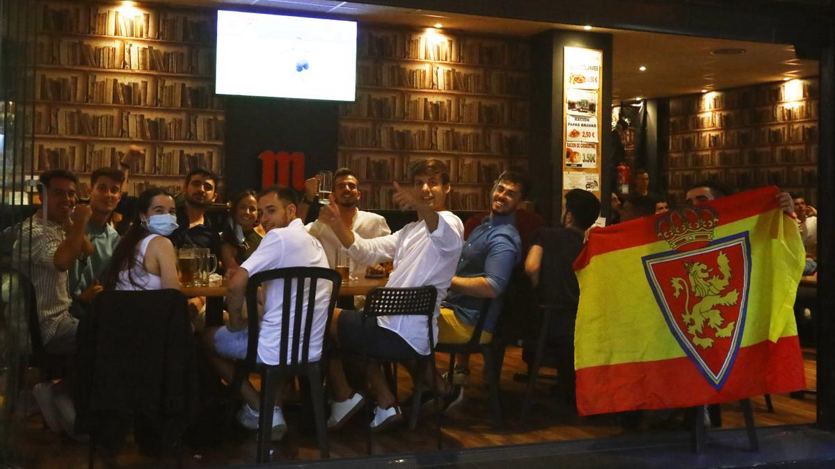 Un grupo de aficionados observa el partido junto a una bandera de España con el escudo del Real Zaragoza.